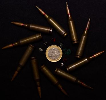 Rifle ammo with a lot of gemstones around one euro coin on black background. Symbolizes the war for money and one of the world's problems.