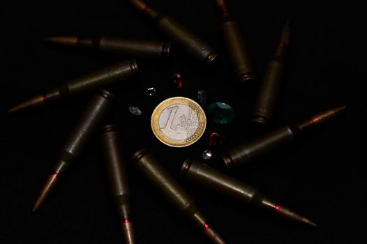 Rifle ammo with a lot of gemstones around one euro coin on black background. Symbolizes the war for money and one of the world's problems.
