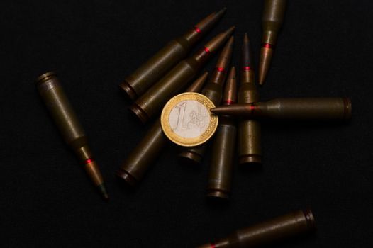 Rifle ammo around one euro coin on black background. Symbolizes the war for money and one of the world's problems.