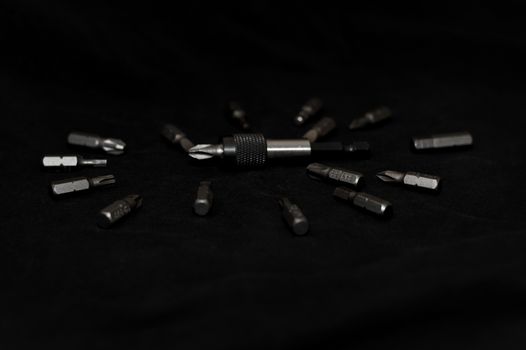 Tool carbon steel bits on black background in dark key style. Bit holder in center and bits around bit holder.