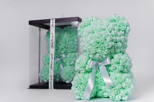Green teddy bear toy of foamirane roses. The same teddy in clear box with black paper cover on background. White stripe on teddy neck. Stock photo isolated on white background. Gift on holiday for women.