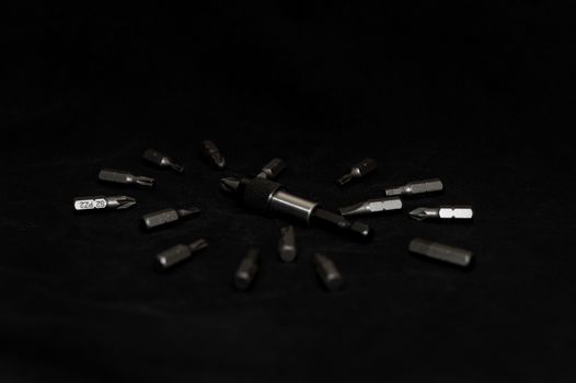Tool carbon steel bits on black background in dark key style. Bit holder in center and bits around bit holder.