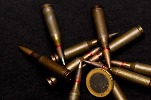 Rifle ammo and one euro coin on black background. Symbolizes the war for money and one of the world's problems.