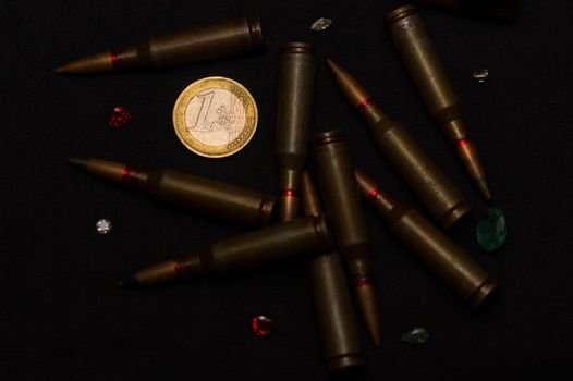 Rifle ammo around one euro coin wigh gemstones on black background. Symbolizes the war for money and one of the world's problems.