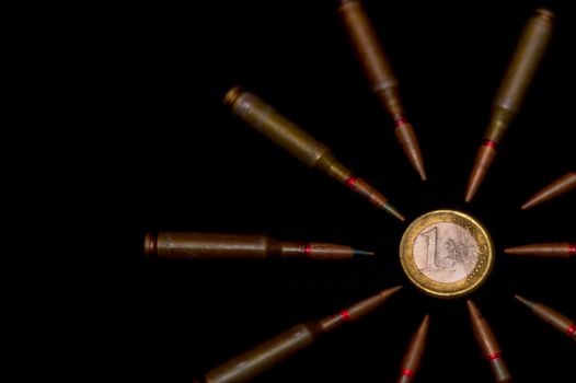 Rifle ammo around one euro coin on black background. Symbolizes the war for money and one of the world's problems.