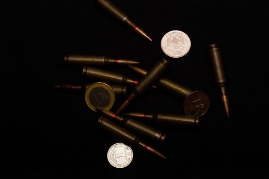 One euro, one Russian ruble and Ukrainian hryvna coins with rifle military ammo on black background. Symbolizes war for money- biggest problem in world.