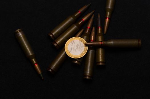 Rifle ammo around one euro coin on black background. Symbolizes the war for money and one of the world's problems.