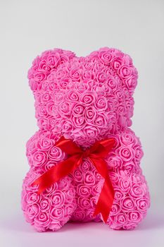 Pink teddy bear toy of foamirane roses. Red stripe on teddy neck. Stock photo isolated on white background. Gift on holiday for women.