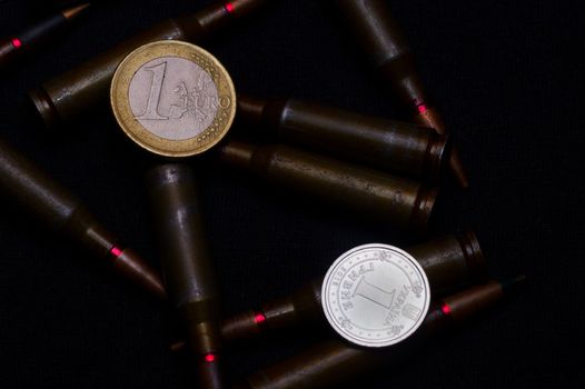 One euro and Ukrainian hryvna coins with rifle military ammo on black background. Symbolizes war for money- biggest problem in world.