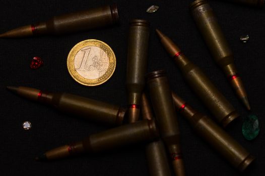 Rifle ammo around one euro coin wigh gemstones on black background. Symbolizes the war for money and one of the world's problems.