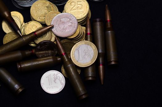 One euro, Russian ruble and small Ukrainian coins with rifle military ammo on black background. Symbolizes war for money- biggest problem in world.
