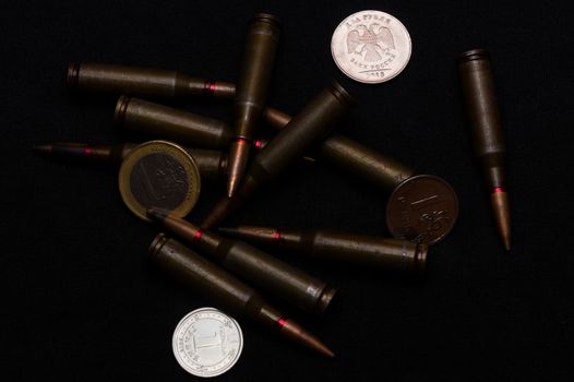 One euro, one Russian ruble and Ukrainian hryvna coins with rifle military ammo on black background. Symbolizes war for money- biggest problem in world.