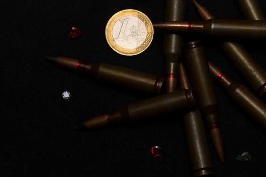 Rifle ammo around one euro coin wigh gemstones on black background. Symbolizes the war for money and one of the world's problems.