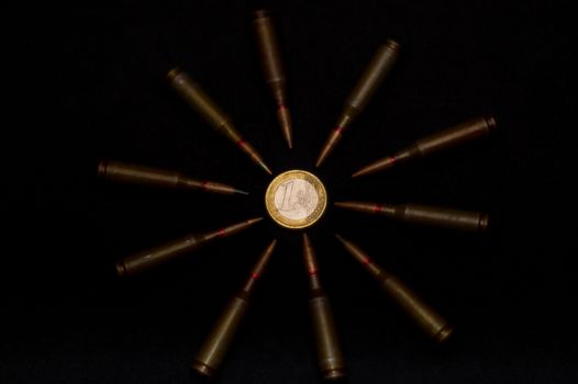 Rifle ammo around one euro coin on black background. Symbolizes the war for money and one of the world's problems.