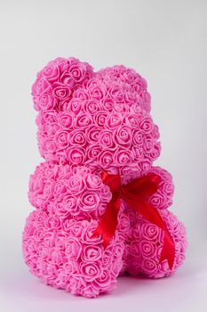 Pink teddy bear toy of foamirane roses. Red stripe on teddy neck. Stock photo isolated on white background. Gift on holiday for women.