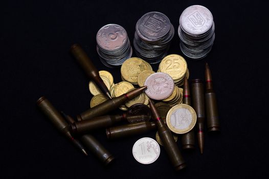 One euro, Russian ruble and small Ukrainian coins with rifle military ammo on black background. Symbolizes war for money- biggest problem in world.