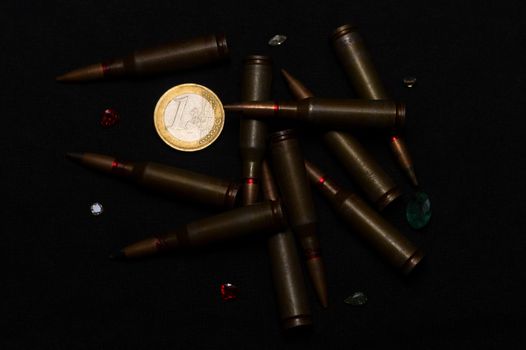 Rifle ammo around one euro coin wigh gemstones on black background. Symbolizes the war for money and one of the world's problems.