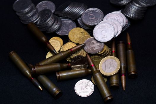 One euro, Russian ruble and small Ukrainian coins with rifle military ammo on black background. Symbolizes war for money- biggest problem in world.
