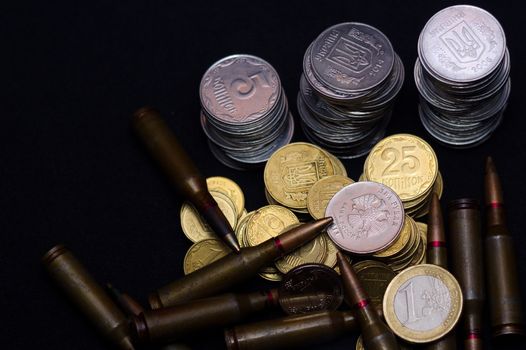 One euro, Russian ruble and small Ukrainian coins with rifle military ammo on black background. Symbolizes war for money- biggest problem in world.