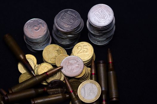 One euro, Russian ruble and small Ukrainian coins with rifle military ammo on black background. Symbolizes war for money- biggest problem in world.