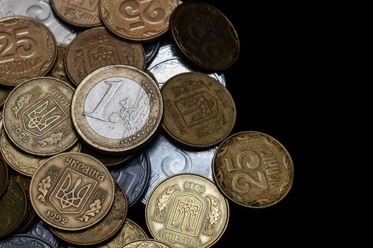Ukrainian coins with one euro coin isolated on black background. Close-up view. Coins are located at the left side of frame. A conceptual image.