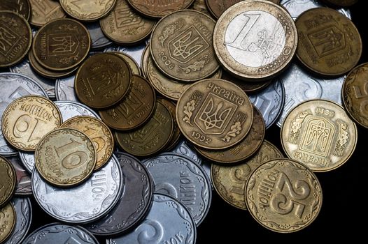 Ukrainian coins with one euro coin isolated on black background. Close-up view. Coins are located at center of frame. A conceptual image.