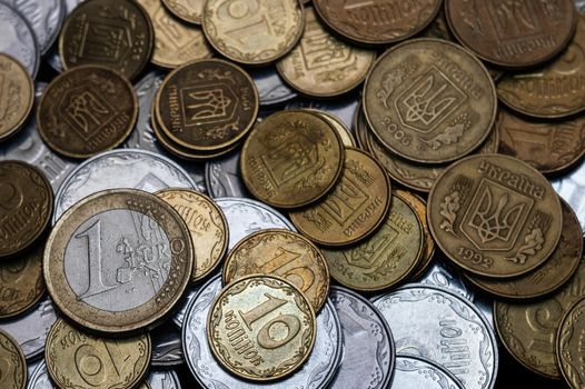 Ukrainian coins with one euro coin isolated on black background. Close-up view. Coins are located at center of frame. A conceptual image.