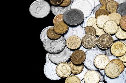Ukrainian coins with one euro coin isolated on black background. Euro coin is uncolored. Close-up view. Coins are located at the right side of frame. A conceptual image.