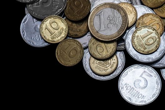 Ukrainian coins with one euro coin isolated on black background. Close-up view. Coins are located at the right side of frame. A conceptual image.