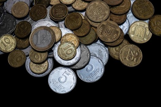 Ukrainian coins with one euro coin isolated on black background. Close-up view. Coins are located at the upper side of frame. A conceptual image.
