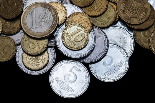 Ukrainian coins with one euro coin isolated on black background. Close-up view. Coins are located at the upper side of frame. A conceptual image.