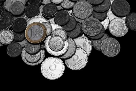 Ukrainian coins with one euro coin isolated on black background. Black and white image.  Euro coin is colored. Close-up view. Coins are located at the upper side of frame. A conceptual image.