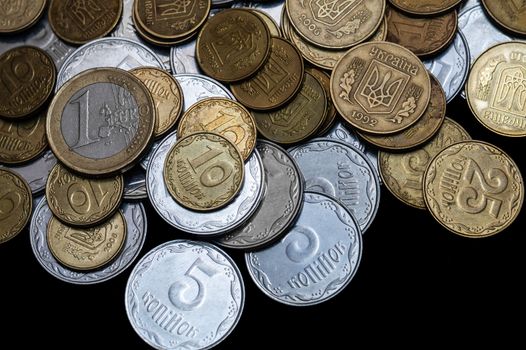 Ukrainian coins with one euro coin isolated on black background. Close-up view. Coins are located at the upper side of frame. A conceptual image.