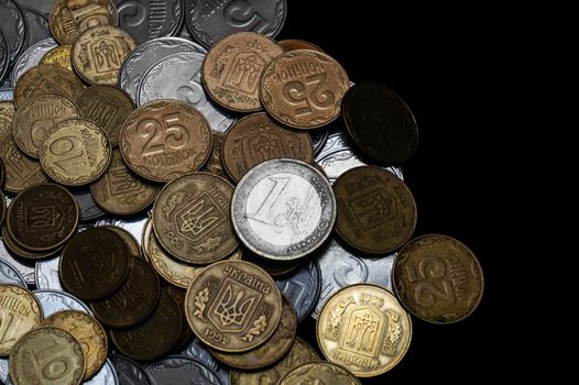 Ukrainian coins with one euro coin isolated on black background. Euro coin is uncolored. Close-up view. Coins are located at the left side of frame. A conceptual image.