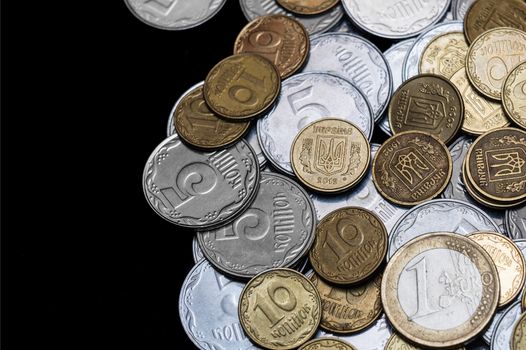 Ukrainian coins with one euro coin isolated on black background. Close-up view. Coins are located at the right side of frame. A conceptual image.