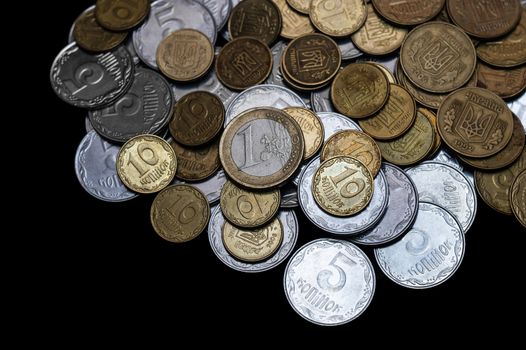 Ukrainian coins with one euro coin isolated on black background. Close-up view. Coins are located at the upper side of frame. A conceptual image.