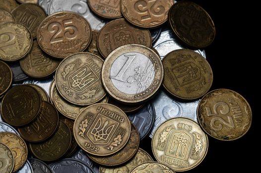 Ukrainian coins with one euro coin isolated on black background. Close-up view. Coins are located at center of frame. A conceptual image.