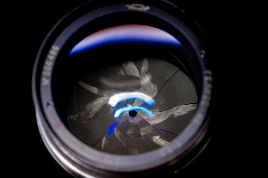 Lens aperture low light photo closeup. Blue traces on glass. Aperture blades is dirty and partially damaged. Stock photo isolated on black background.