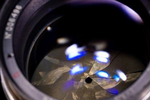 Lens aperture low light photo closeup. Blue traces on glass. Aperture blades is dirty and partially damaged.