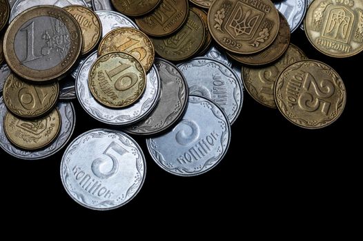 Ukrainian coins with one euro coin isolated on black background. Close-up view. Coins are located at the upper side of frame. A conceptual image.