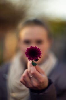 Pretty young girl holds dark purple flower in front of her. Girl is very defocused, soft focus on hand.