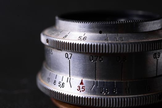 Old vintage lens scales symbols closeup. Photo with blurred gray background. Aperture symbols and focusing distance signs on lens.