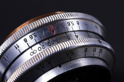 Old vintage lens scales symbols closeup view. Photo with blurred gray background. Aperture symbols and focus distance sign on lens.