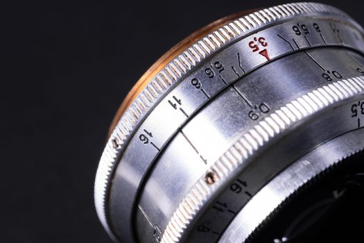 Old vintage lens scales symbols closeup view. Photo with blurred gray background. Aperture symbols and focus distance sign on lens.