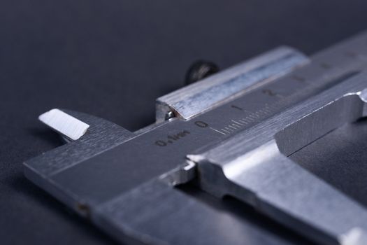 Vintage steel caliper tool closeup. Scale in focus. Tool in very good condition. Scale in metric units, milimeter step. Stock photo on blurred gray background.