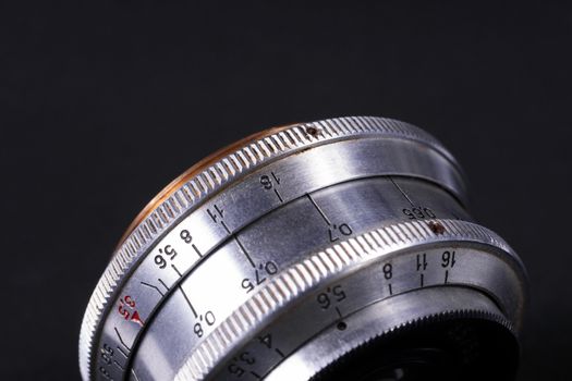 Old vintage lens scales symbols closeup view. Photo with blurred gray background. Aperture symbols and focus distance sign on lens.