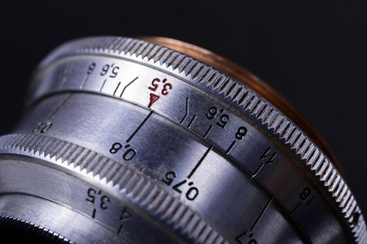 Old vintage lens scales symbols closeup view. Photo with blurred gray background. Aperture symbols and focus distance sign on lens.
