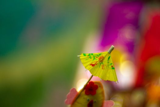 Yellow cocktail paper umbrella on colorful blurred defocused background.