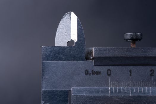 Vintage steel caliper tool closeup. Caliper tips and scale in focus. Tool in very good condition. Scale in metric units, milimeter step. Stock photo on blurred gray background.