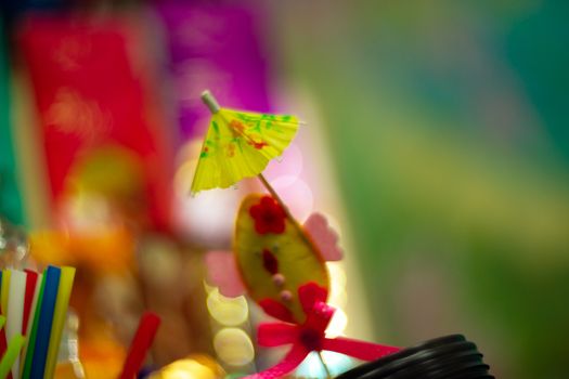 Yellow cocktail paper umbrella on colorful blurred defocused background.
